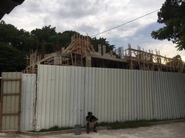 Construction site from outside the fence.  Man sitting at base of fence.